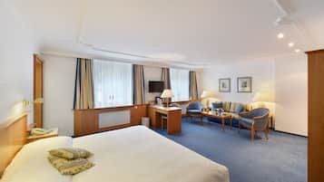 A hotel room with a large bed, a desk with a chair, a sofa, and a television.