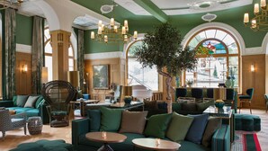 A spacious lounge area with green sofas, round tables, and a large tree. - Hotel Walther (Pontresina)