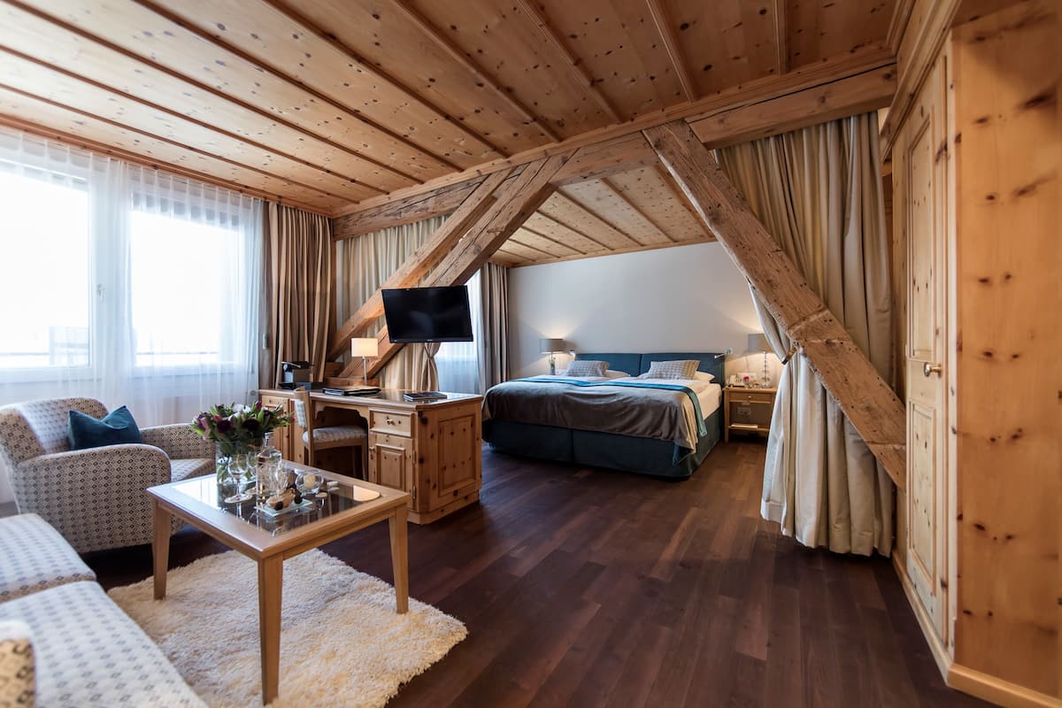 Ein gemütliches Zimmer mit Holzbalkendecke, einem Bett, einem Schreibtisch mit Fernseher und einem Sofa.