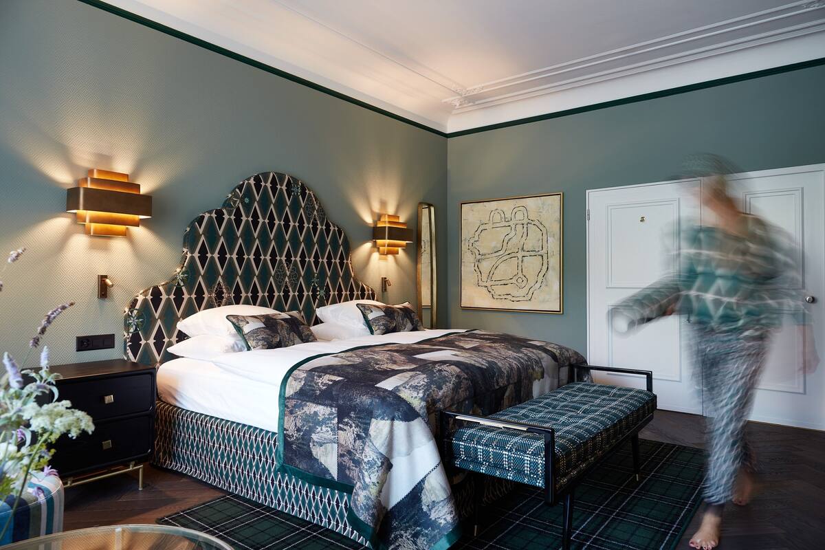 Ein Schlafzimmer mit einem Bett, Nachttischen, einer Bank und Wandbildern.