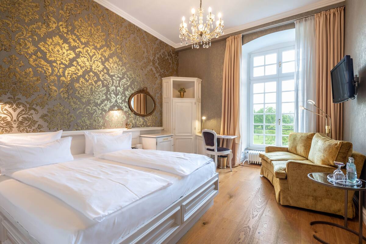 Une chambre d’hôtel avec un grand lit, un canapé, une télévision et une fenêtre avec des rideaux.