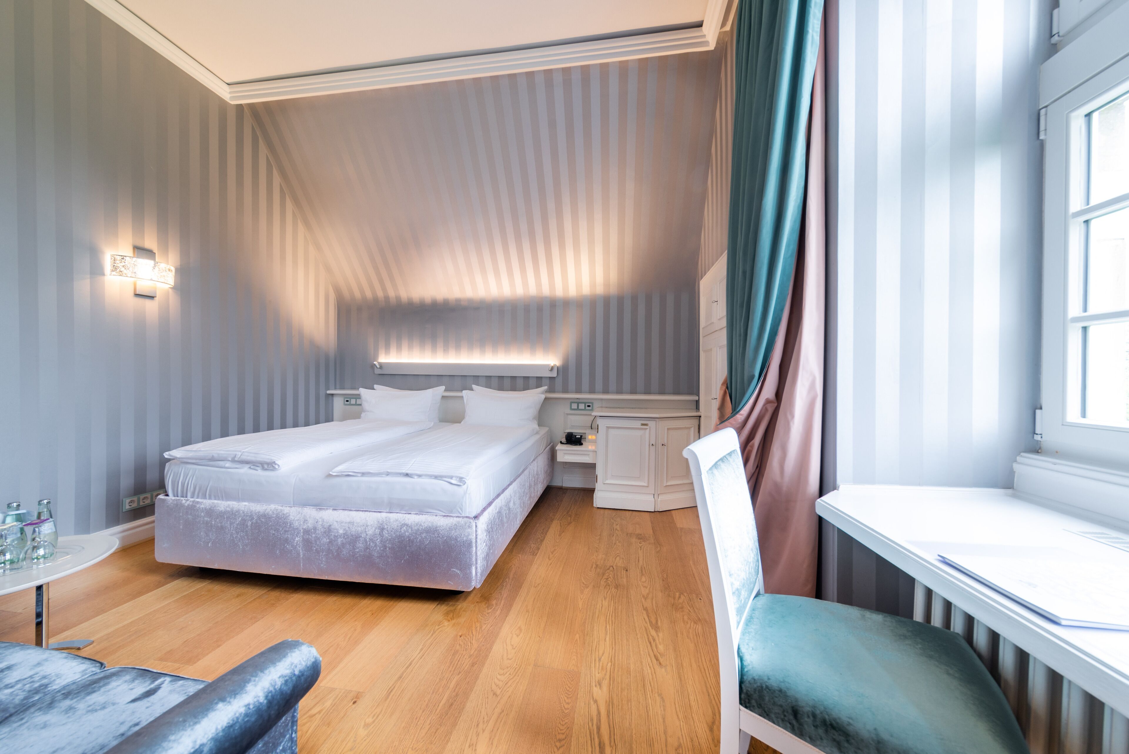 A hotel room with a bed, bedside table, lamp, and a window with curtains.