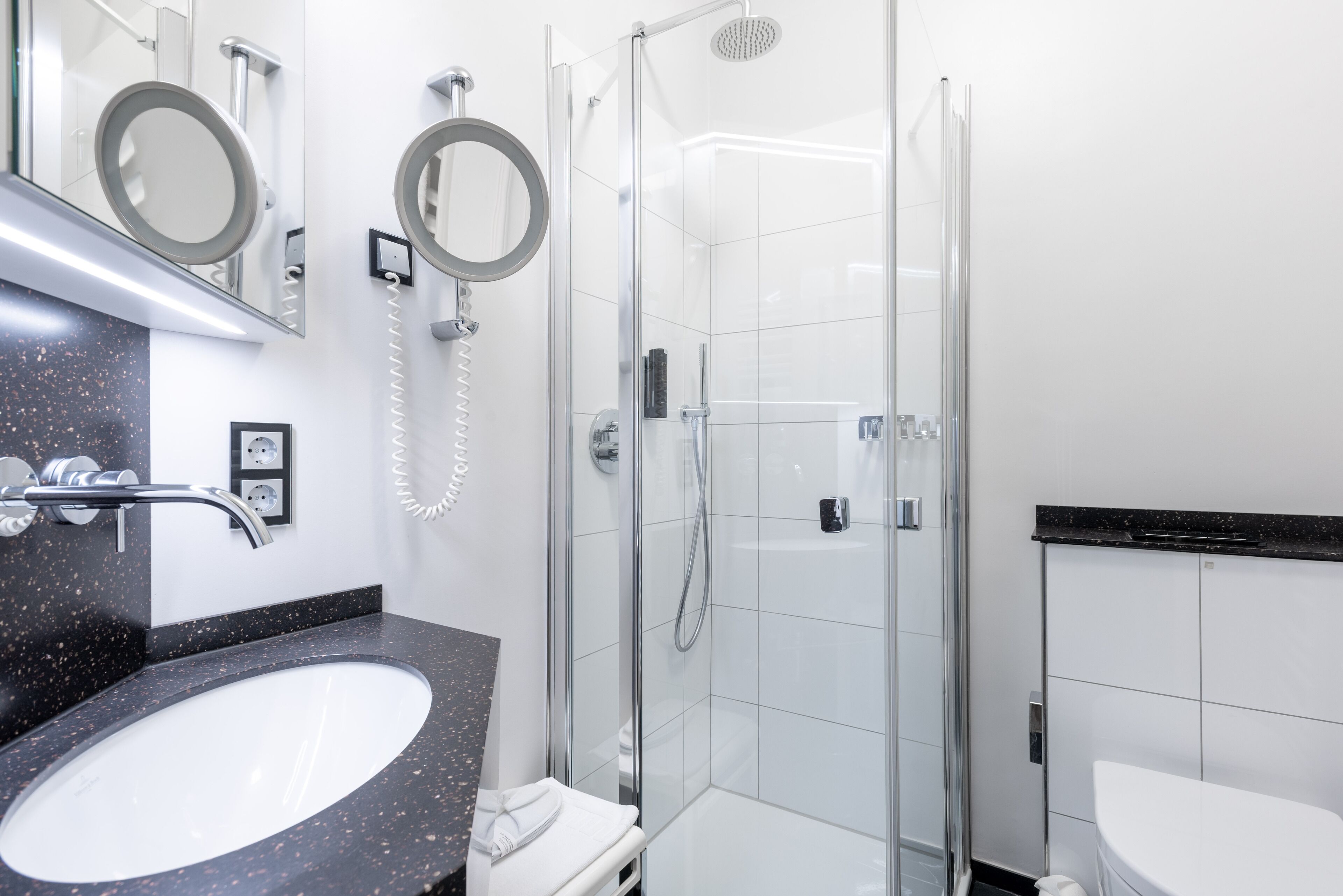 A modern bathroom with a glass-enclosed shower, a white sink with a black countertop, and two wall-mounted mirrors.