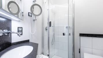 A modern bathroom with a glass-enclosed shower, a white sink with a black countertop, and two wall-mounted mirrors.