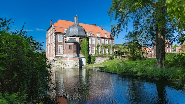 Il s’agit d’un bâtiment historique, doté d’un toit recouvert de tuiles rouges, d’un dôme central et d’une petite tour. Il est situé au bord d’une rivière paisible, entouré d’une végétation luxuriante.