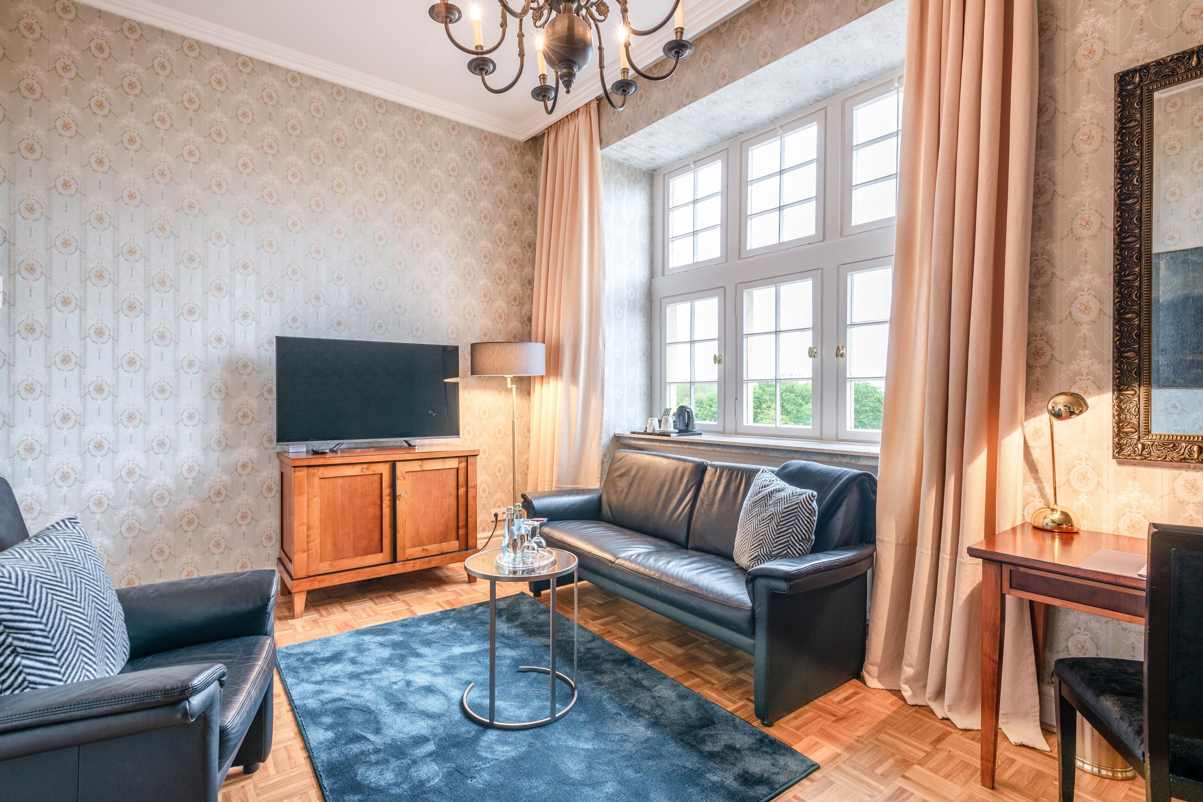 A living room with a sofa, a TV, a wooden cabinet, a small table, and a window with curtains.