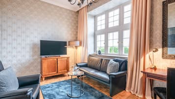 A living room with a sofa, a TV, a wooden cabinet, a small table, and a window with curtains.
