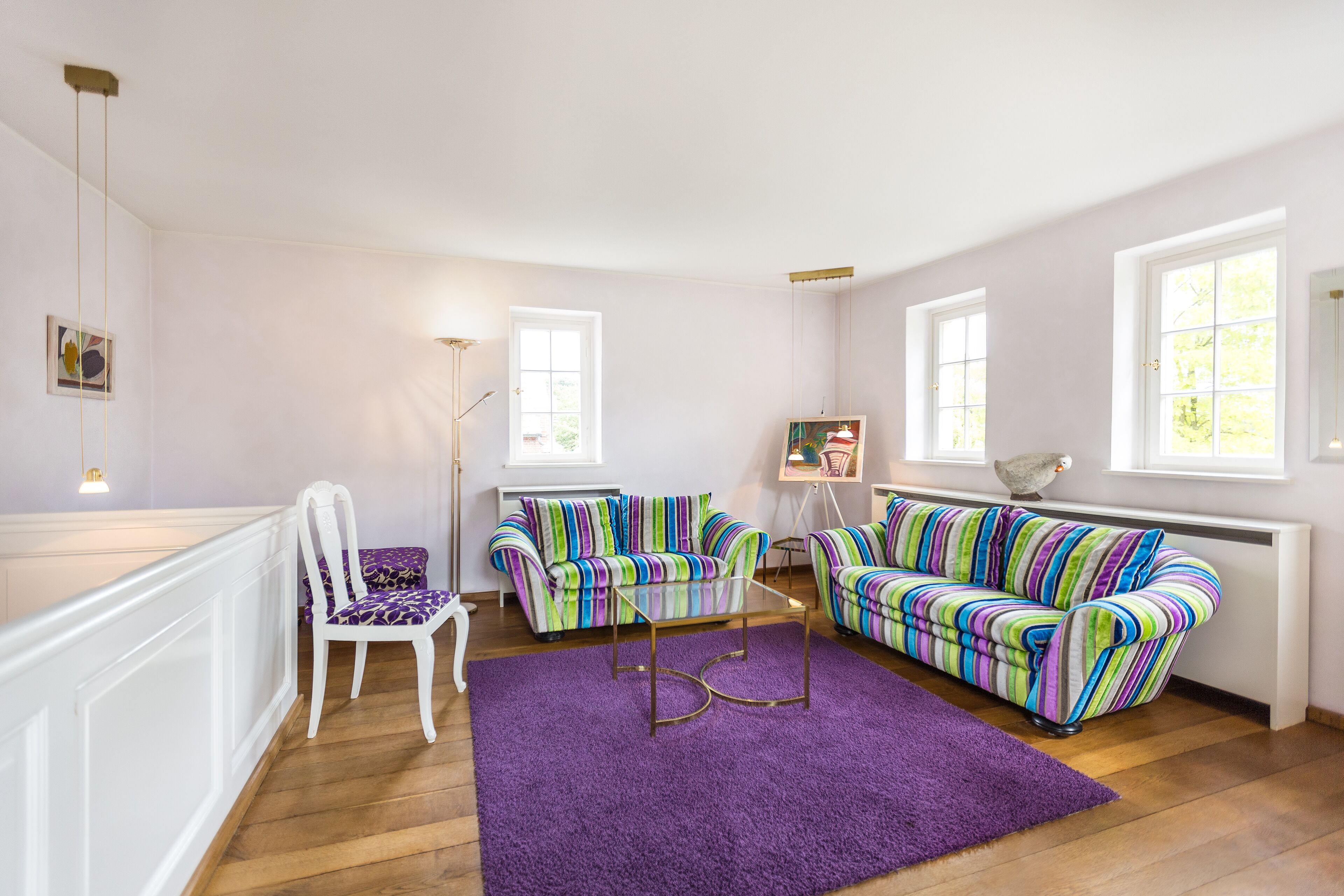 A room with two striped sofas, a purple rug, and a white chair.
