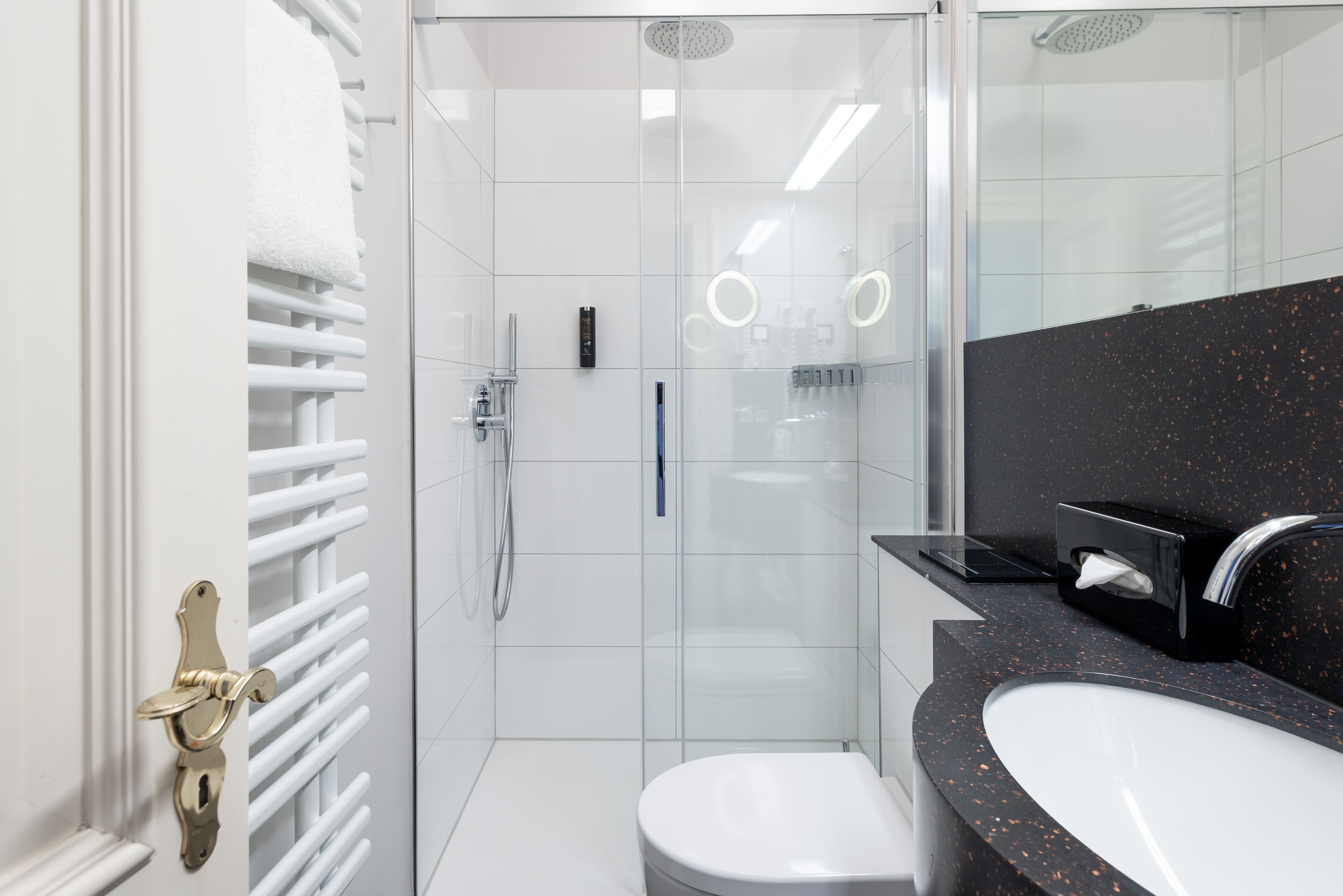 Un baño moderno con cabina de ducha de vidrio, inodoro blanco y encimera negra con lavabo.