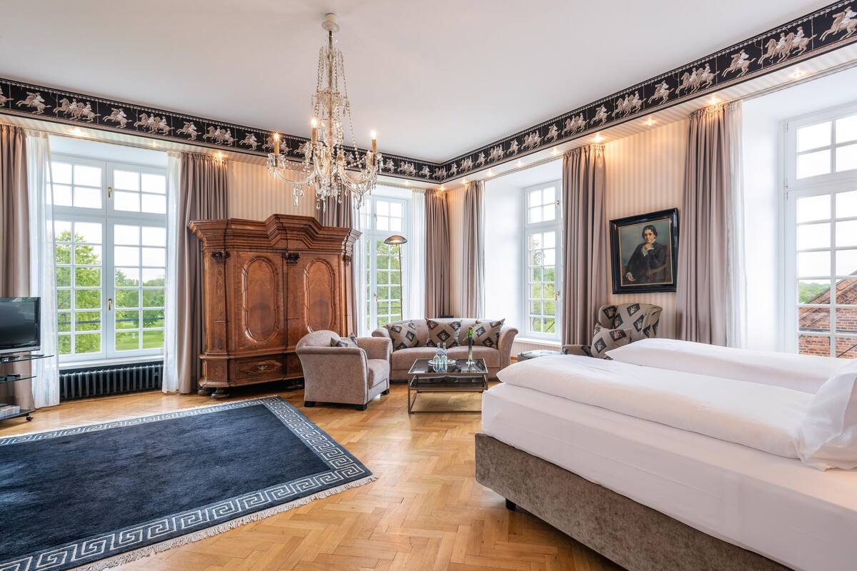 Une pièce spacieuse avec un grand lit, une armoire en bois, un canapé et un lustre.