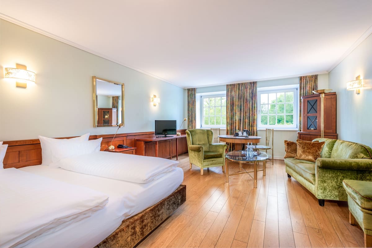 Une chambre d’hôtel avec un grand lit, un bureau avec un ordinateur, un fauteuil vert et un canapé.