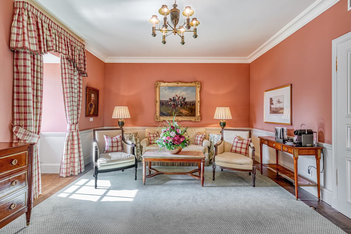 Ein Zimmer mit einer Sofagarnitur, einem Tisch mit floraler Dekoration und einer Kristallleuchter.