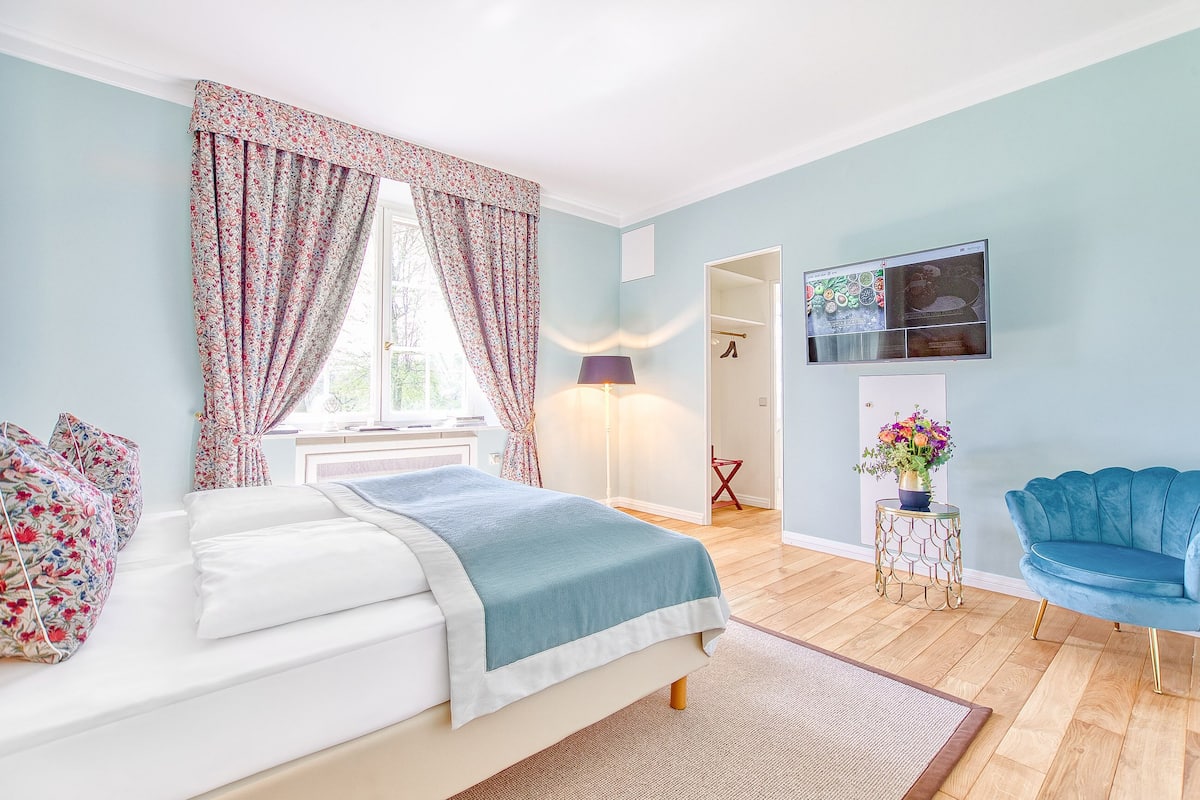 Ein Schlafzimmer mit Bett, Fernseher, blauem Sofa und einem Fenster mit Vorhängen.