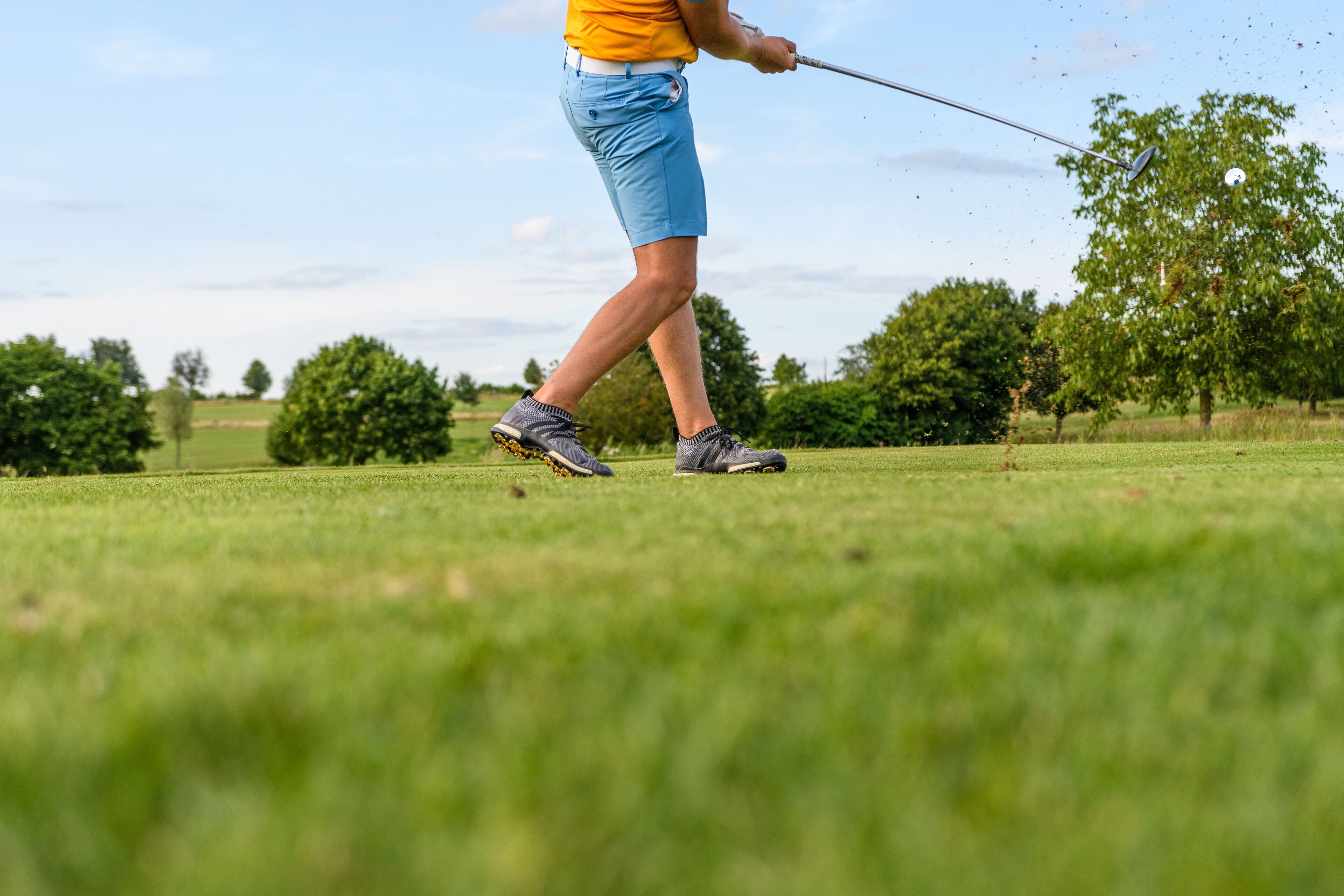 Una persona con camisa amarilla y pantalones cortos azules caminando en un campo de golf.