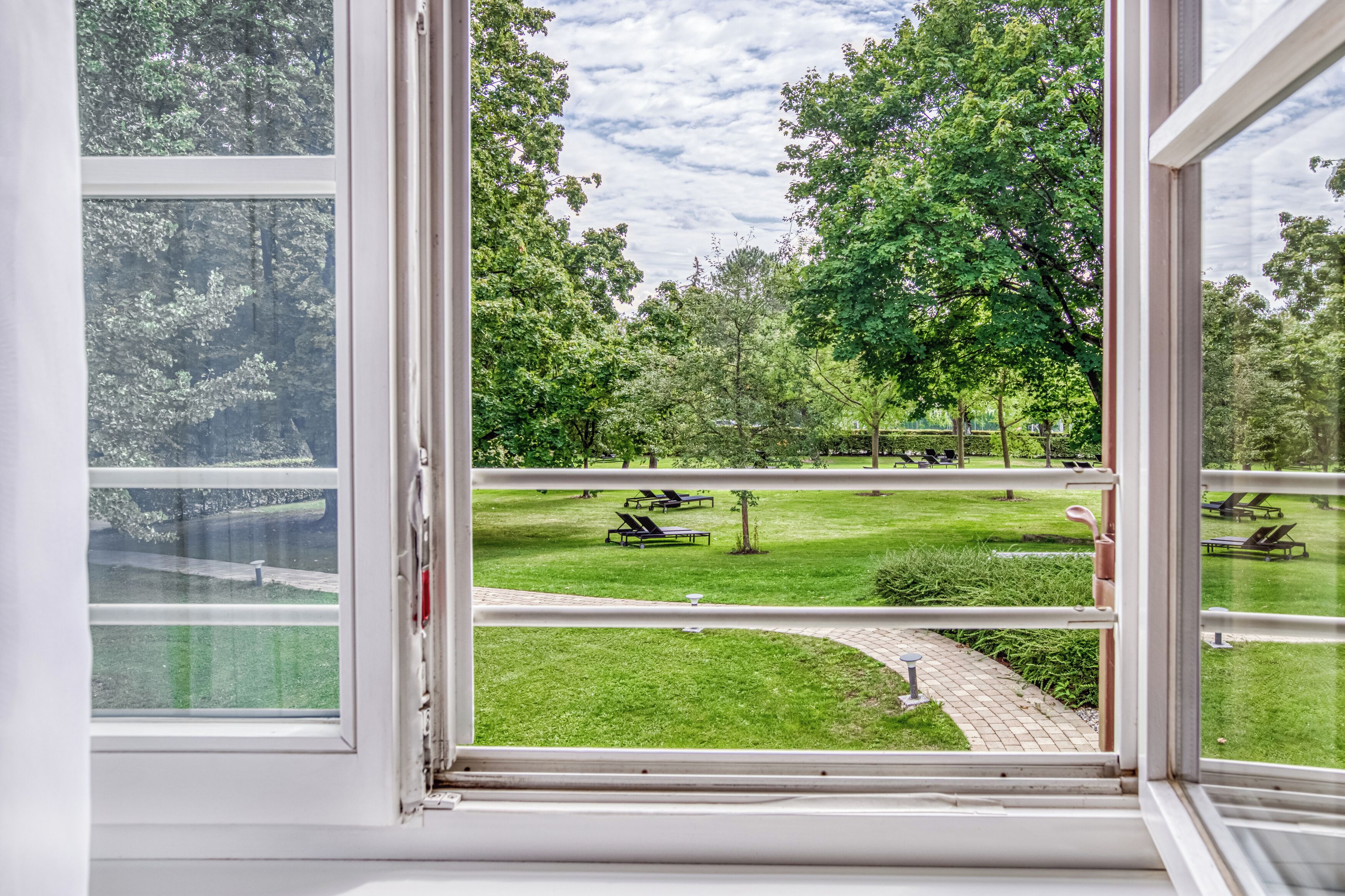 Blick aus einem Fenster auf einen Park mit Rasen, Bäumen und Liegestühlen.
