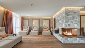 A modern living room with a stone fireplace, a sofa, two armchairs, and a large window with curtains. - Wald & Schlosshotel Friedrichsruhe (Zweiflingen-Friedrichsruhe)