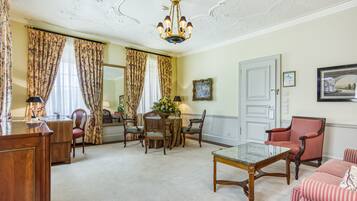 A well-furnished living room with a wooden coffee table, a red striped armchair, and a dining area with floral curtains and a flower vase.