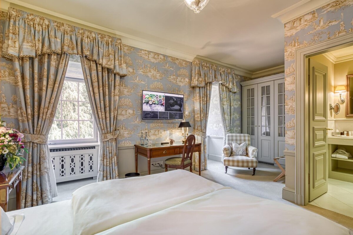 A hotel room with a large bed, a desk, a chair, and a wardrobe.