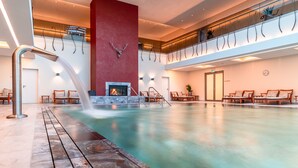A spacious indoor pool with a waterfall feature, a fireplace, and multiple seating areas. - Wald & Schlosshotel Friedrichsruhe (Zweiflingen-Friedrichsruhe)