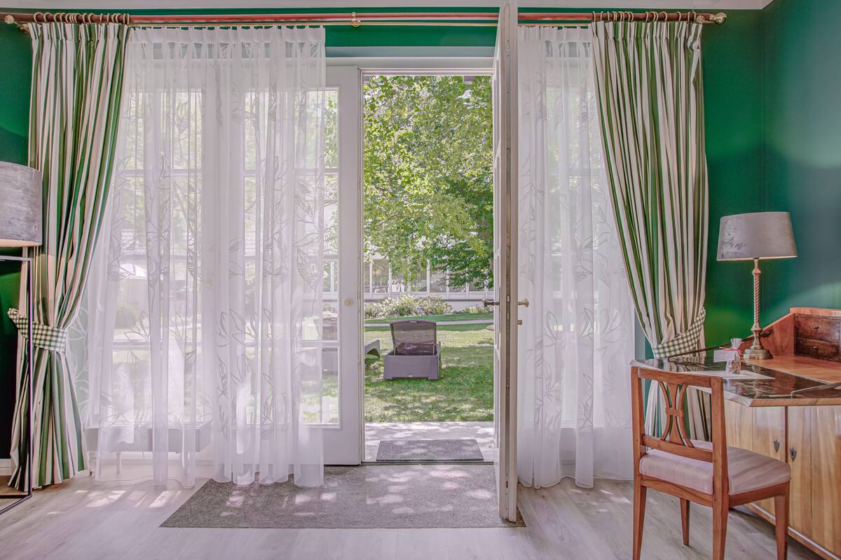 Ein Zimmer mit Blick auf einen Garten durch eine Glastür, ein Holzstuhl und ein Tisch mit einer Lampe.