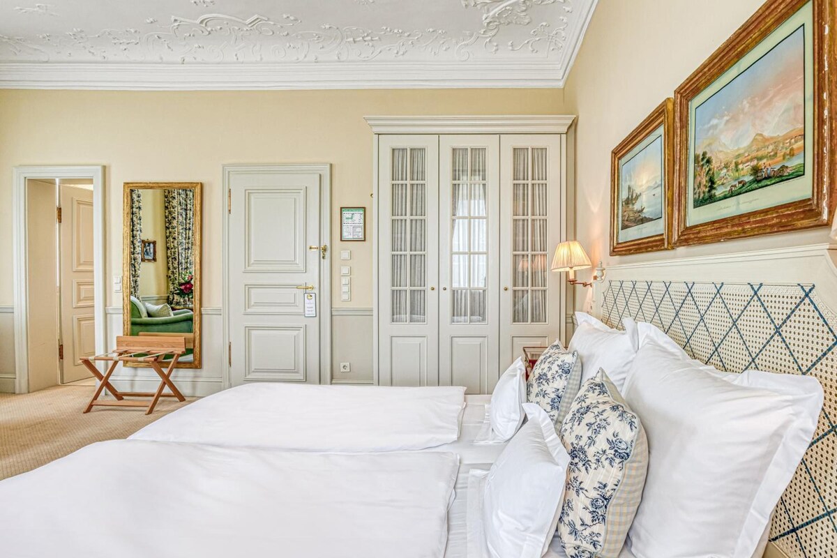 A hotel room with a large bed, a sitting area with a green sofa, and a painting on the wall.