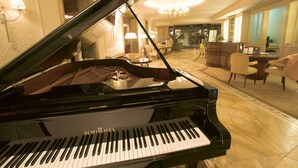 A grand piano in a well-lit, elegantly furnished room with a chandelier, seating area, and a reception desk. - Wald & Schlosshotel Friedrichsruhe (Zweiflingen-Friedrichsruhe)