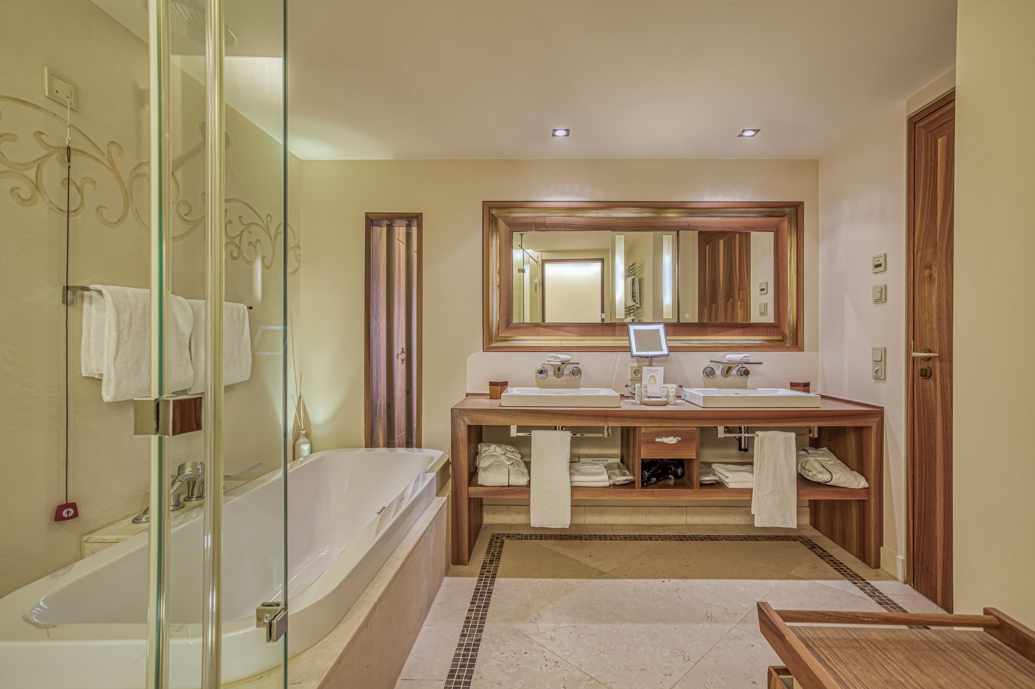 A modern bathroom with a glass-enclosed shower, a large mirror above a wooden vanity with two sinks, and a bathtub.