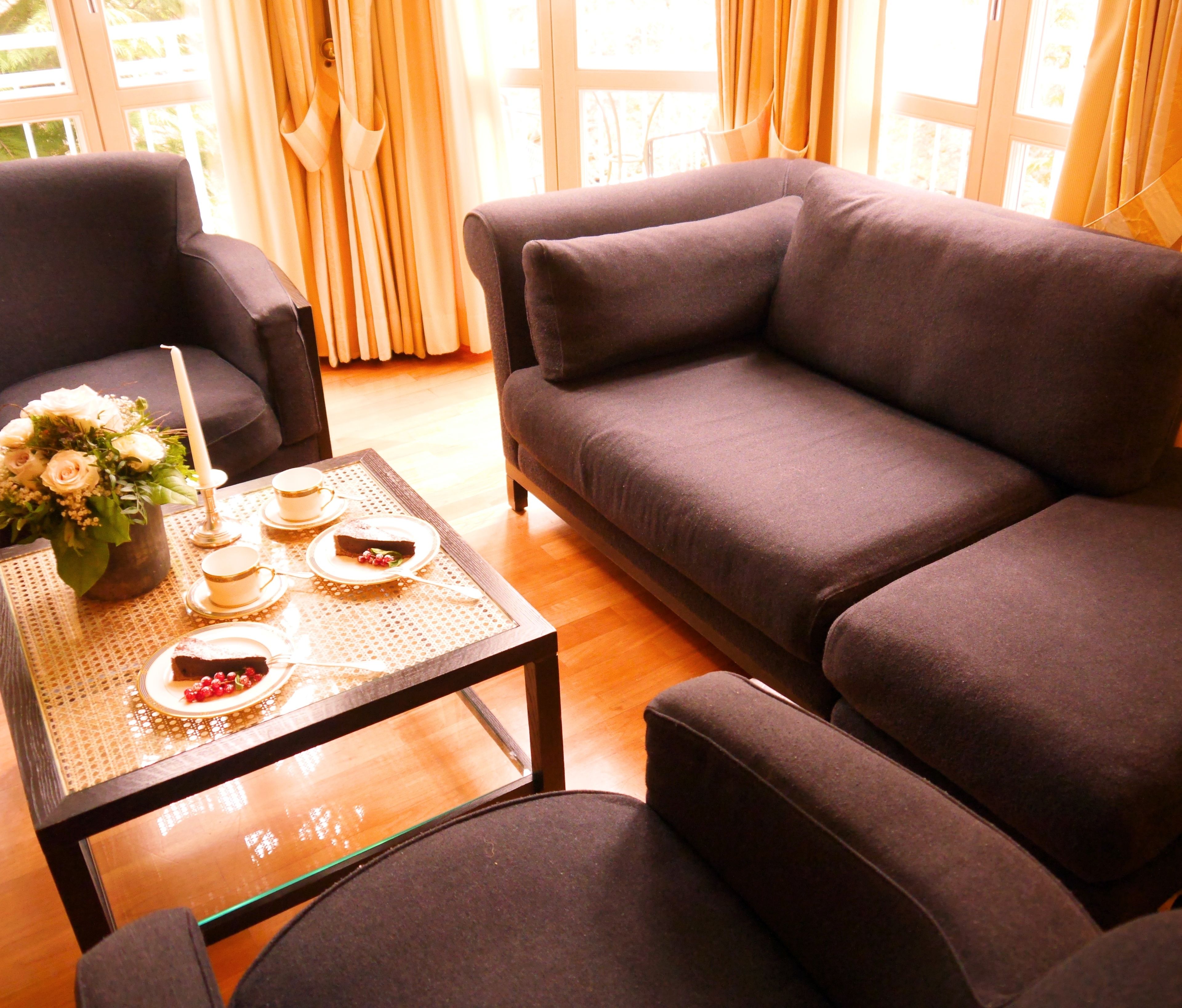 A living room with a dark brown sofa, a matching armchair, and a coffee table with a floral arrangement and a cake.