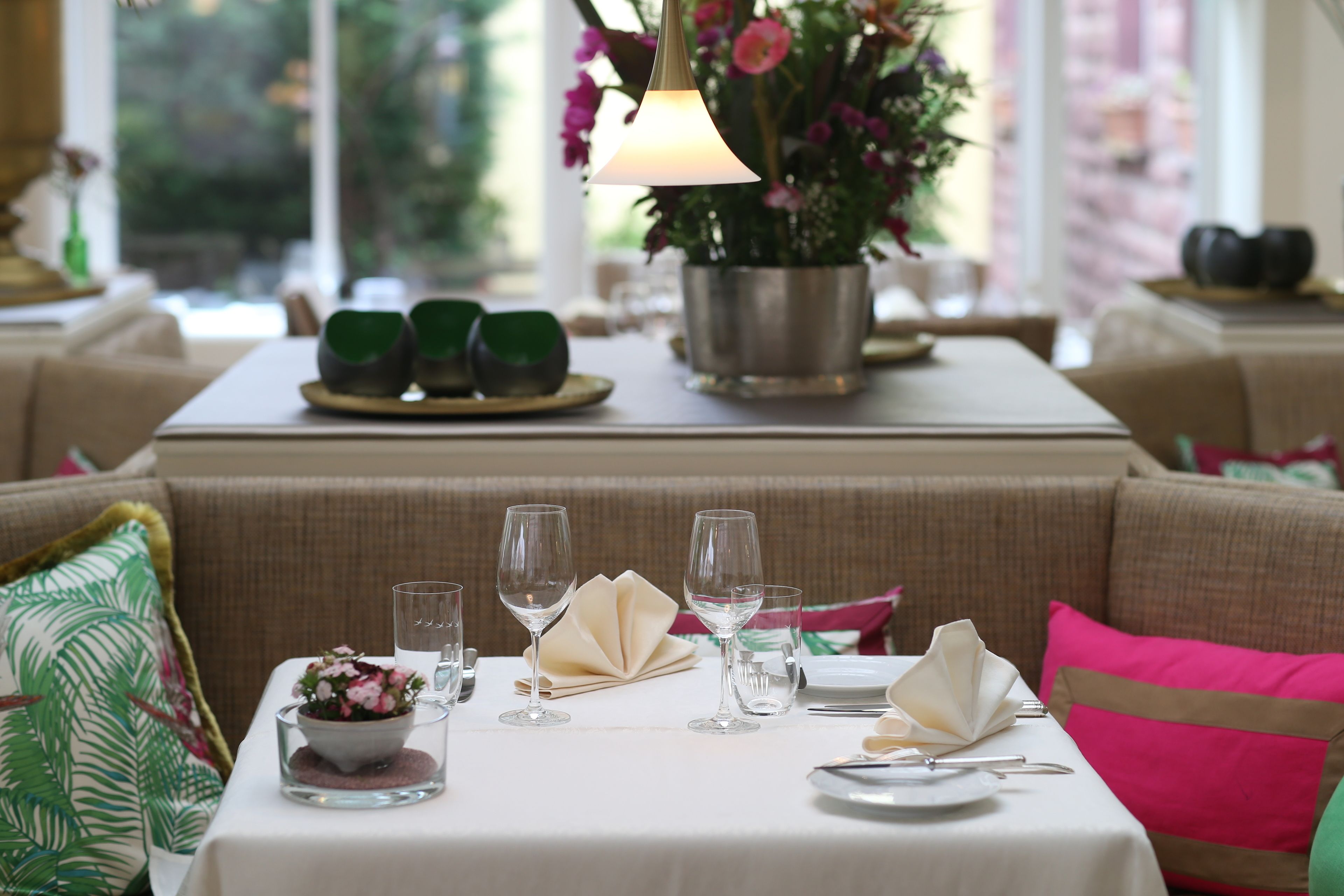 Un comedor con una mesa dispuesta para una comida, que incluye platos, vasos y un centro de mesa con flores.