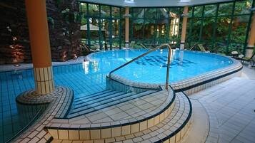 Una piscina interior con suelo de baldosas y una escalera central que baja al agua.
