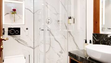 A modern bathroom with a glass-enclosed shower, a white toilet, a marble-tiled floor, and a large mirror above the sink.