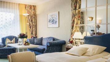 A hotel room with a bed, a sofa, a chair, and a small table with a lamp.