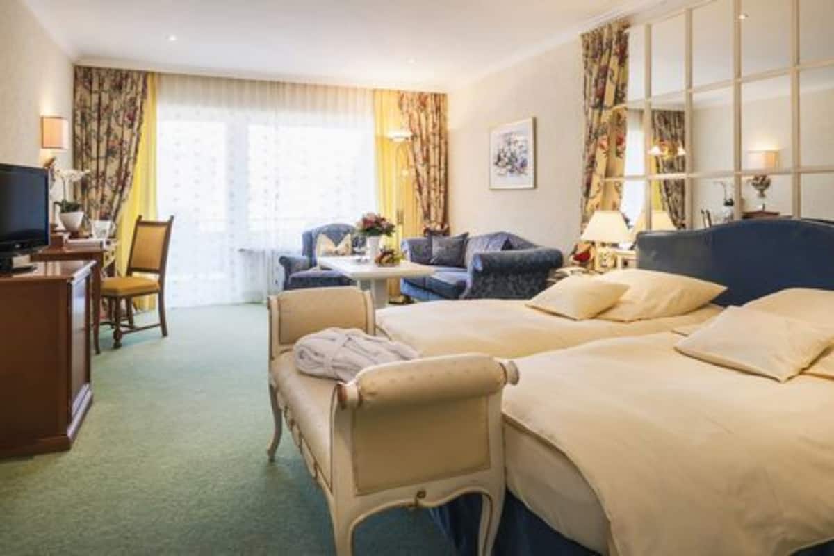A hotel room with two beds, a desk with a chair, a television, and a window with curtains.