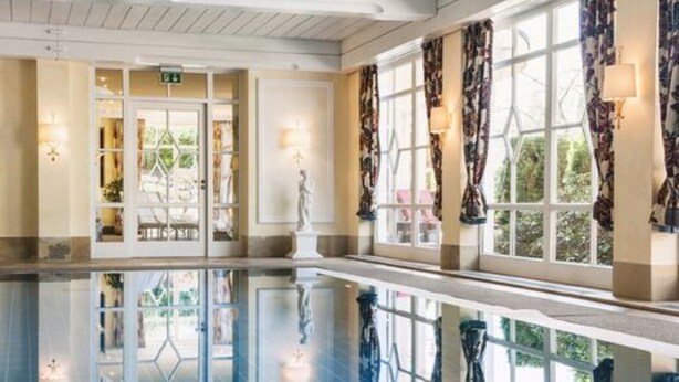 A hotel lobby with a reflective pool, large windows with patterned curtains, and a statue in the center. - Hotel Schwarzmatt (Badenweiler)