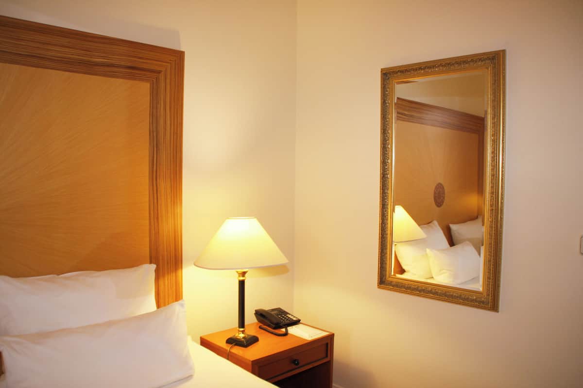 A hotel room with a wooden headboard, a bedside lamp, a nightstand with a phone, and a mirror on the wall.