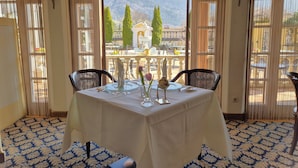A dining area with a table set for two, a view of a mountainous landscape through large windows, and a patterned carpet.