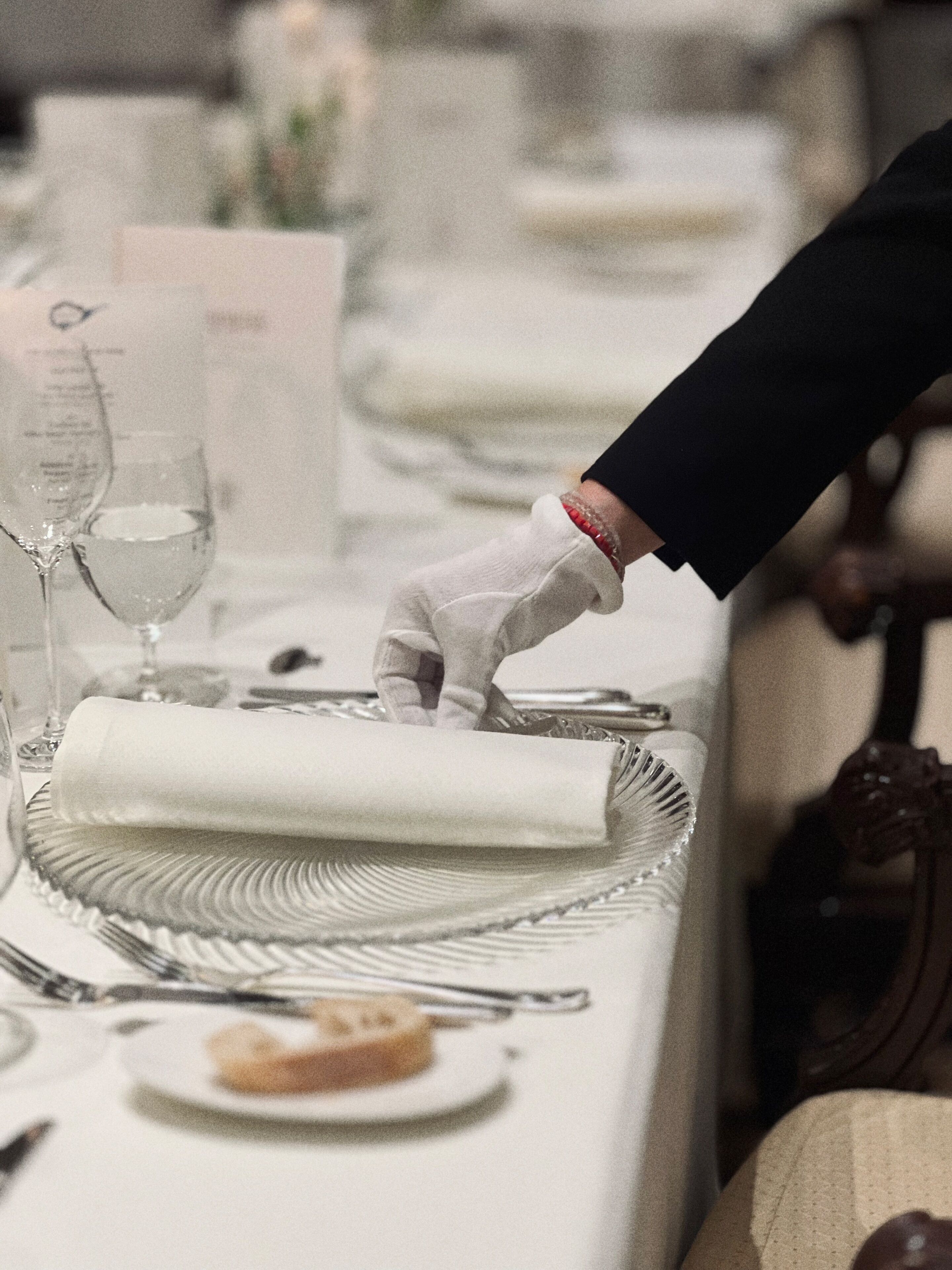 Una mesa dispuesta para una comida formal, con un mantel doblado, un vaso de agua y un plato con un pastel.