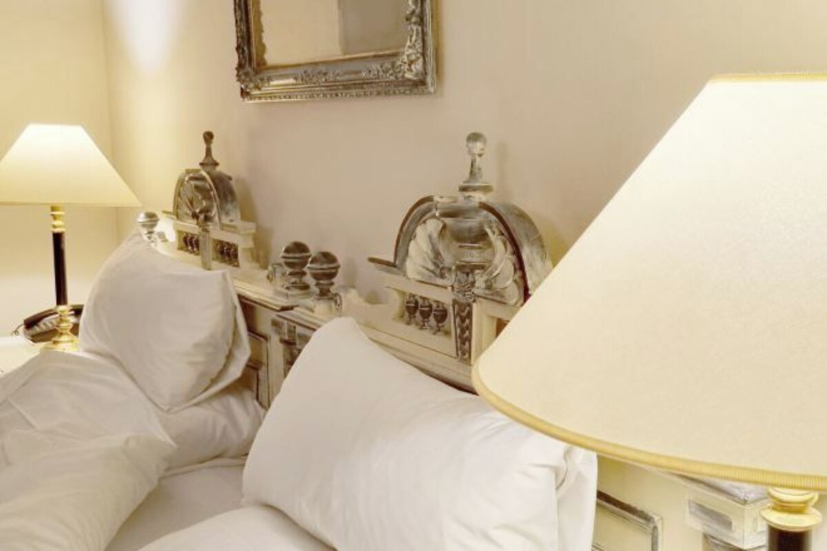 A corner of a room with a white armchair, a lamp, and a decorative cabinet with glassware.