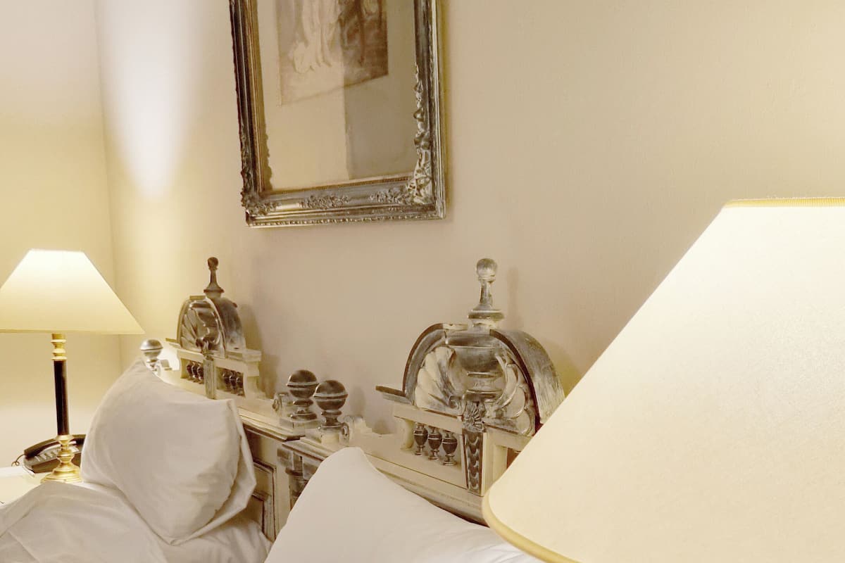 A hotel room with a bed, a nightstand, a lamp, and a mirror.