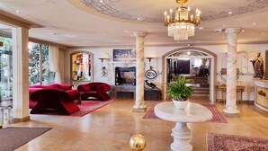 A spacious lobby with a grand chandelier, marble columns, and a red sofa set.
