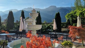 A fountain with a tiered design, surrounded by outdoor seating and tables, with mountains in the background.