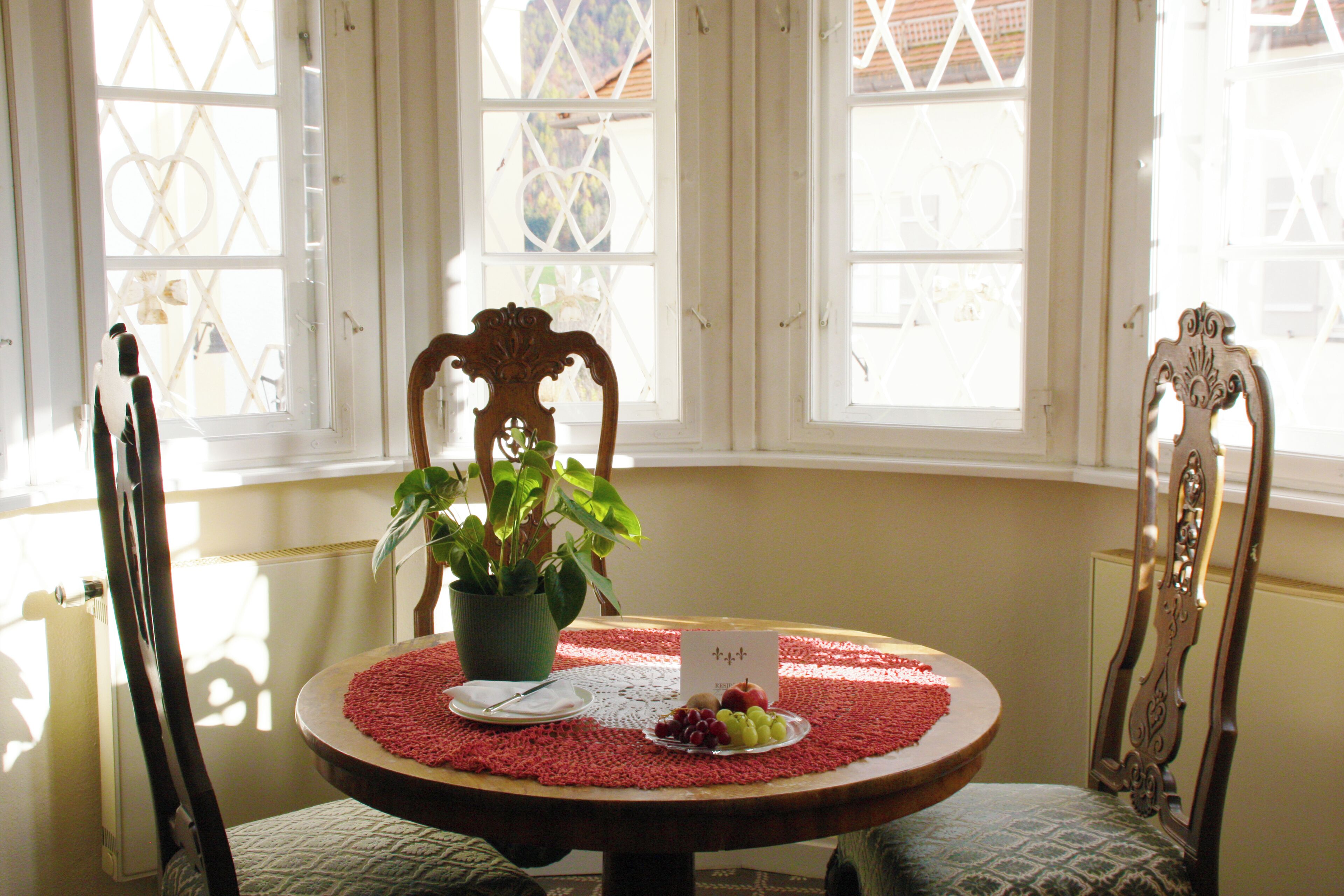 Una mesa de comedor con un mantel individual, un plato de uvas, una planta pequeña en maceta y una tarjeta.