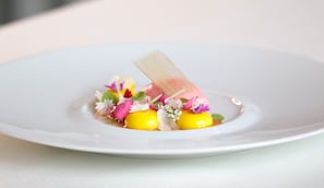 A white plate with a yellow and pink dessert, garnished with flowers and a transparent element. - Boutique Hotel Residenz Winkler (Aschau im Chiemgau)