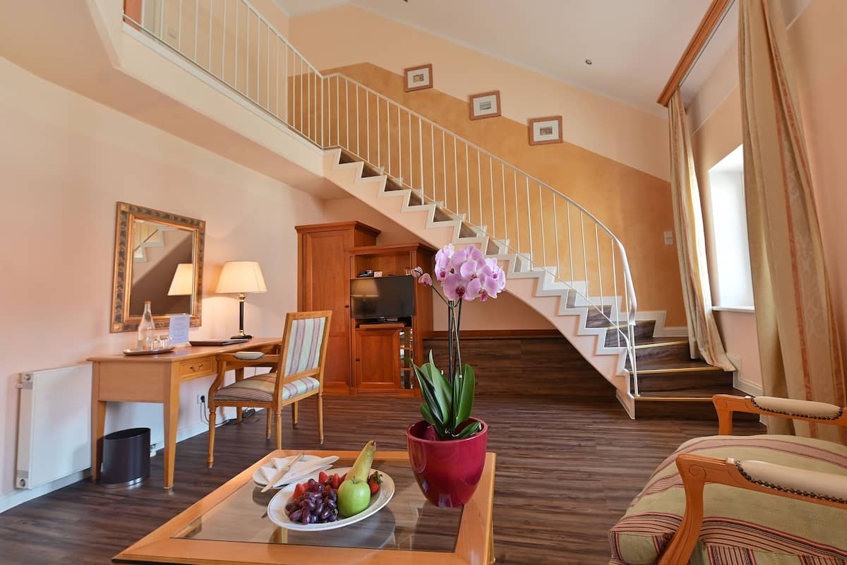 A spacious living room with a wooden staircase, a dining area with a fruit plate, a television, and a potted orchid.