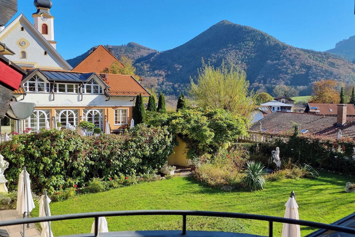 A traditional European-style building with a red-tiled roof, a bell tower, and a well-maintained garden with a lawn and various plants.