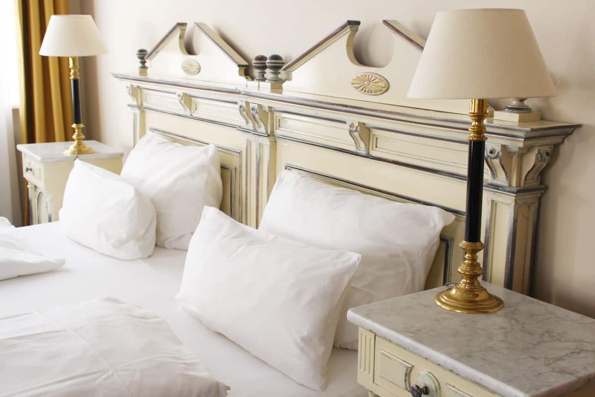 A hotel room with a classic design, featuring a large bed with white linens, two bedside tables with lamps, and a marble nightstand.