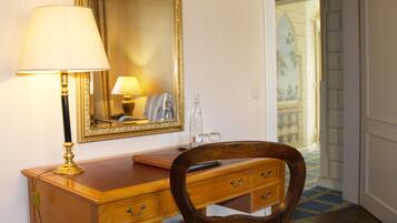 A wooden desk with a lamp, a mirror, and a chair in a room with a door leading to a balcony.