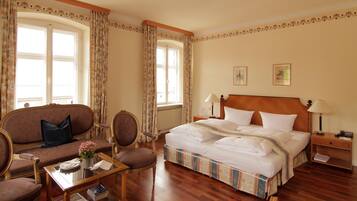 Ein Hotelzimmer mit einem großen Bett, zwei Nachttischen, einem hölzernen Kopfteil, einem Sofa, einem Sessel und einem kleinen Tisch mit Blumen in einer Vase.