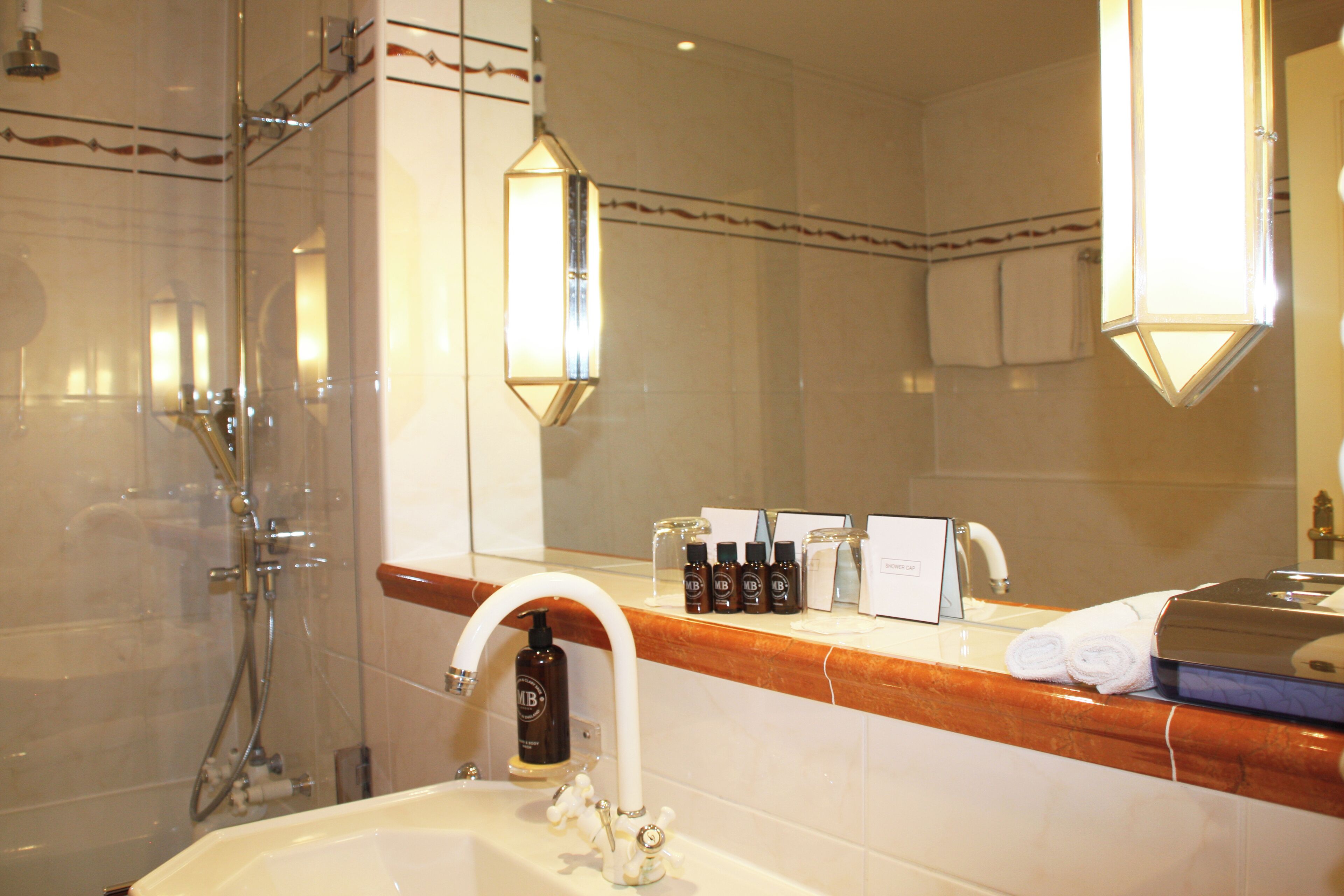 A bathroom with a shower, a sink with a mirror, and toiletries on the countertop.