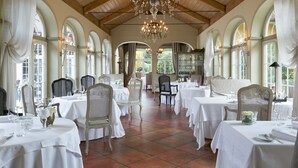 Un comedor con mesas dispuestas para el servicio, candelabros y ventanas de arco.